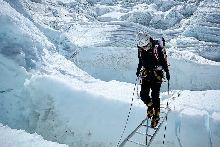 Gabby Kanizay crosses a crevasse on the way up Everest, walking carefully across a ladder.