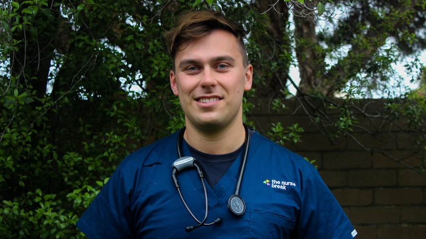 Jackson Heilberg, a young nurse standing outside smiling. He wears hospital scrubs with a stethoscope around his neck.