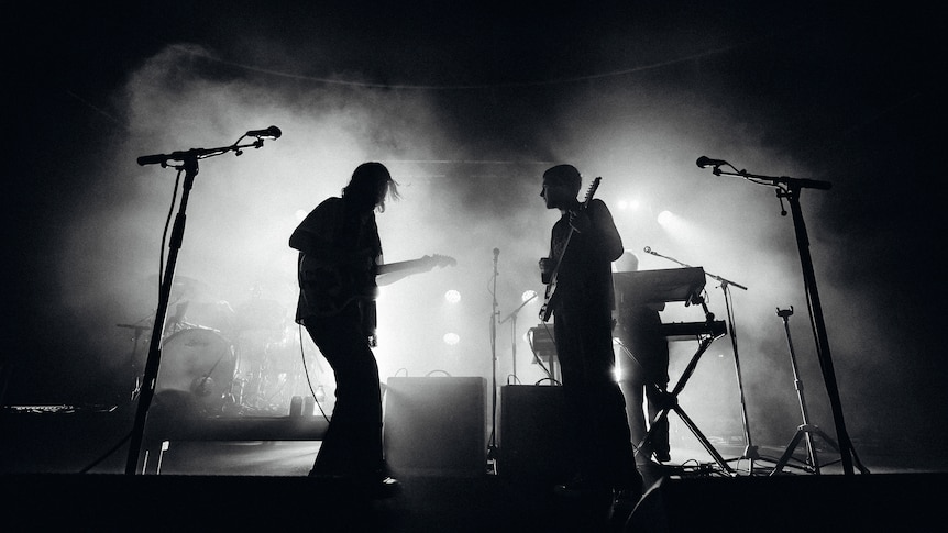 silhouette of two people standing on stage holding guitars with a black and white filter