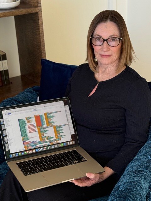 Woman with short hair and glasses holding open a laptop with codes on screens