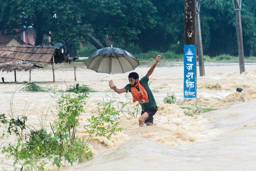A Nepalese man walks through knee-high floodwaters.