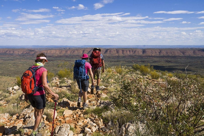 two women and a man walk across a plateau wearing backpacks