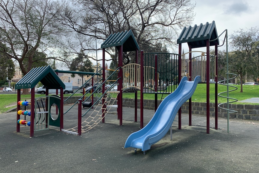 An empty children's playground with a slide and other colourful equipment, in cold daylight.