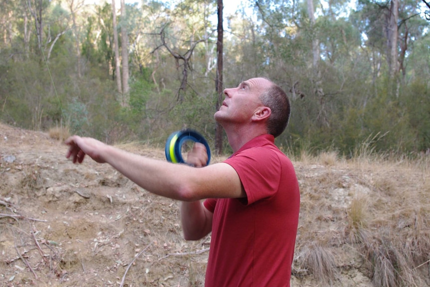 Ecologist John White standing in a drainage channel holding a fishing reel