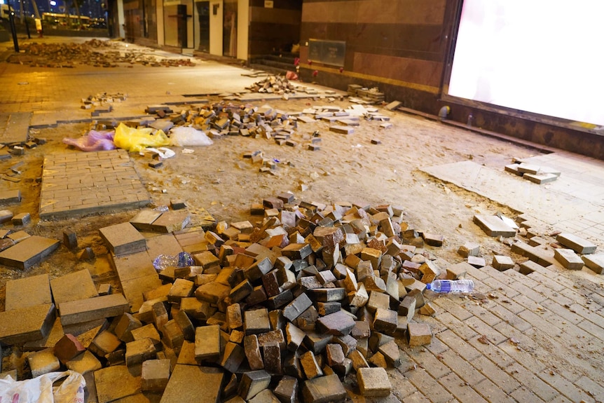 An empty street where hundreds of bricks have been ripped up from the pavement.