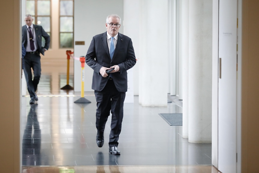 Scott Morrison walking down a white corridor in Parliament House.