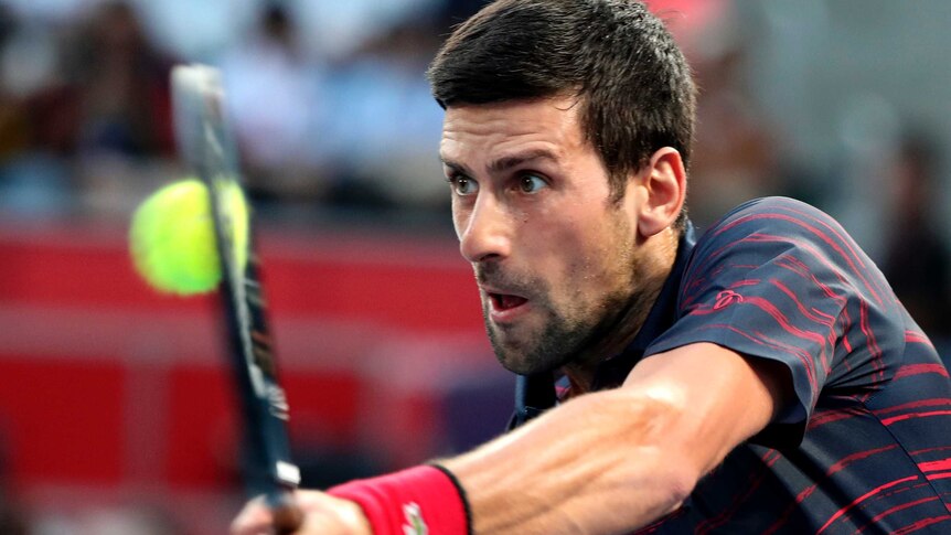 Novak Djokovic looks forward as he leans into a shot, wearing a dark grey shirt with red flashes