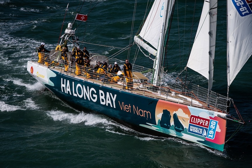 A yacht sails the ocean with crew dressed in yellow sailing gear.