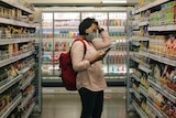 woman stands in supermarket shopping aisle 