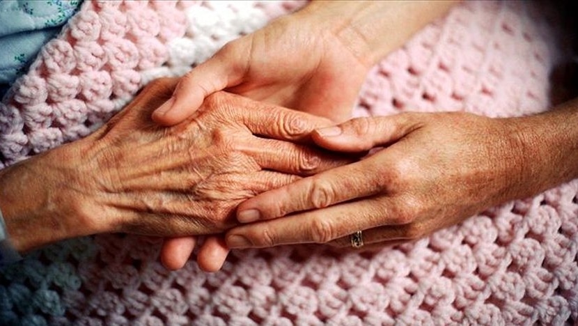 A younger woman's hand holding an elderly patient's hand.