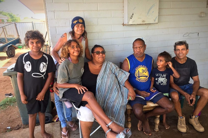 A family in Carnarvon sit on chairs outside their home posing for a picture