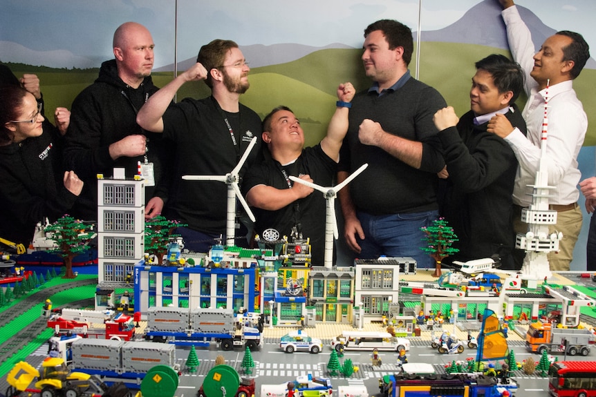 Public servants pose with their fists raised behind a replica city made of Lego blocks