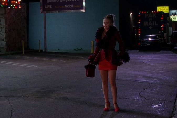 A woman in a car park in a short red dress and a feathered jacket