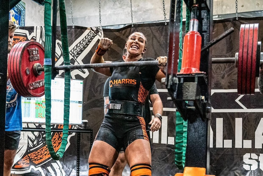 Lily Riley celebrates at a powerlifting competition smiling and punching fist in air