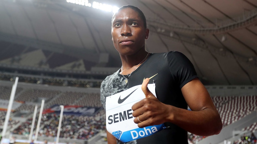 Caster Semenya holds her thumb up looking above the camera with a stadium in the background