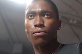 Caster Semenya holds her thumb up looking above the camera with a stadium in the background
