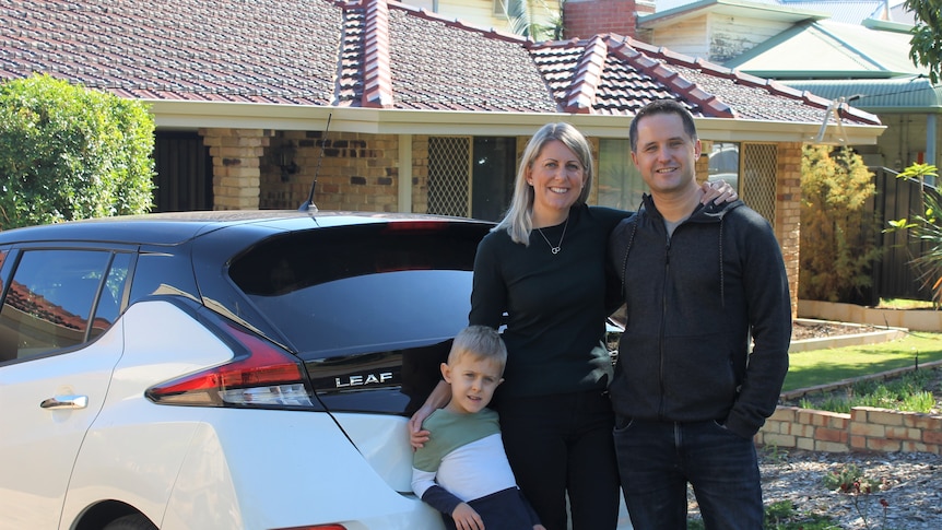 Couple and six year old son standing in front of electric car