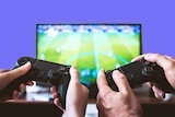 Two people hold video game controllers in front of a television showing scenes from a soccer game.