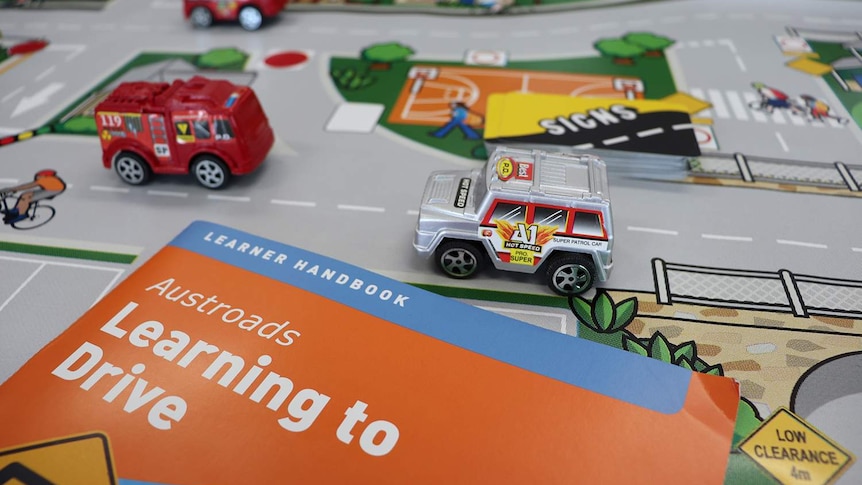 Photo shows top of Austroads learner driver handbook laying on toy road map with toy cars.