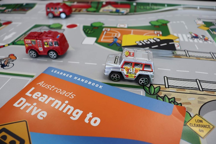 Photo shows top of Austroads learner driver handbook laying on toy road map with toy cars.