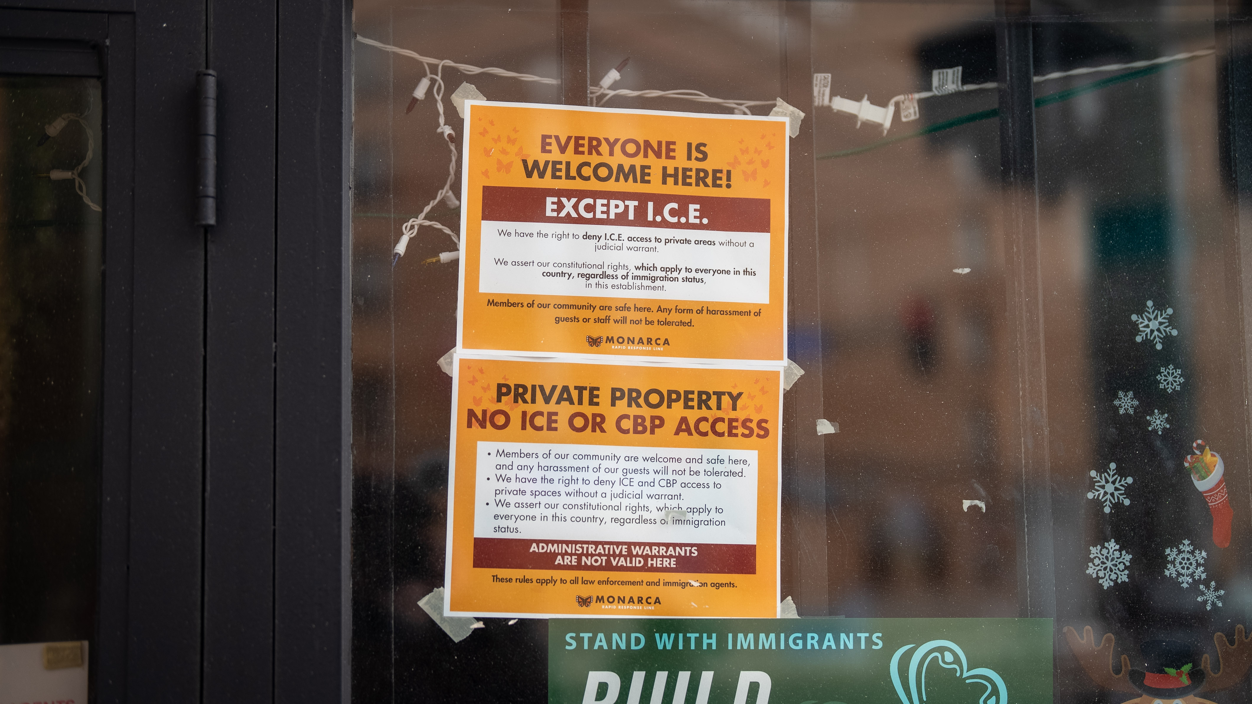 A yellow sign on the door that reads "everyone is welcome here except ICE".