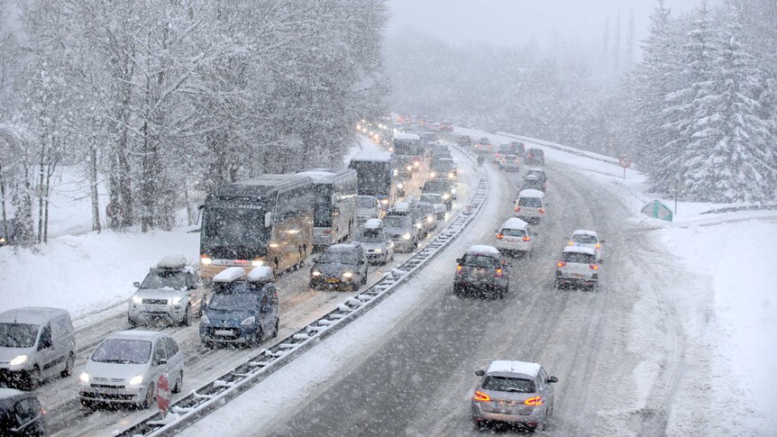 Snow falls as vehicles move bumper-to-bumper along the motorway near Albertville, the French Alps, on December 27, 2014