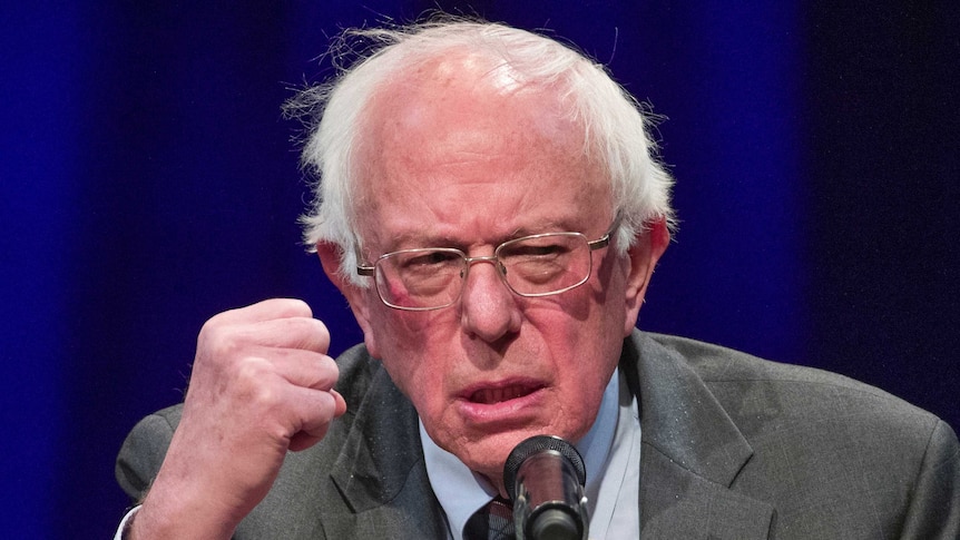 Senator Bernie Sander speaks into a microphone as he raises a fist in the air.