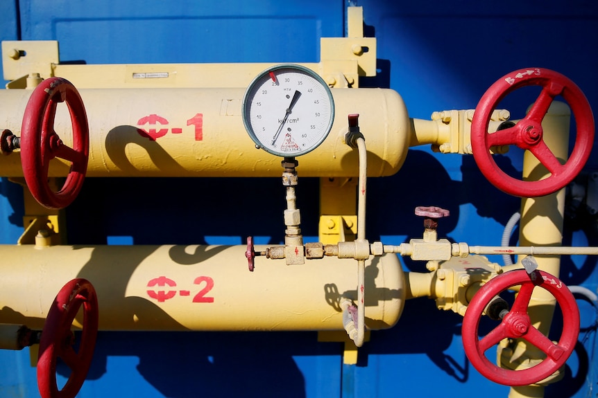 Yellow, red and blue colored valves, pipes and a gauge at a gas compressor station