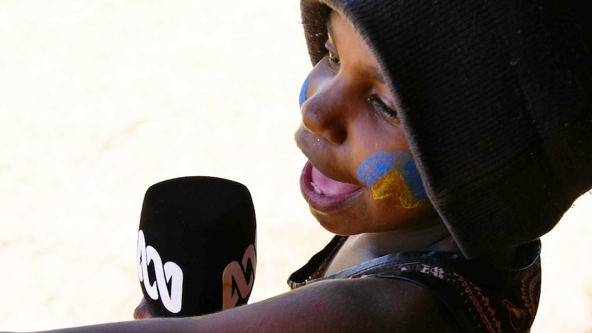 A child from Balgo, Western Australia holds a microphone.