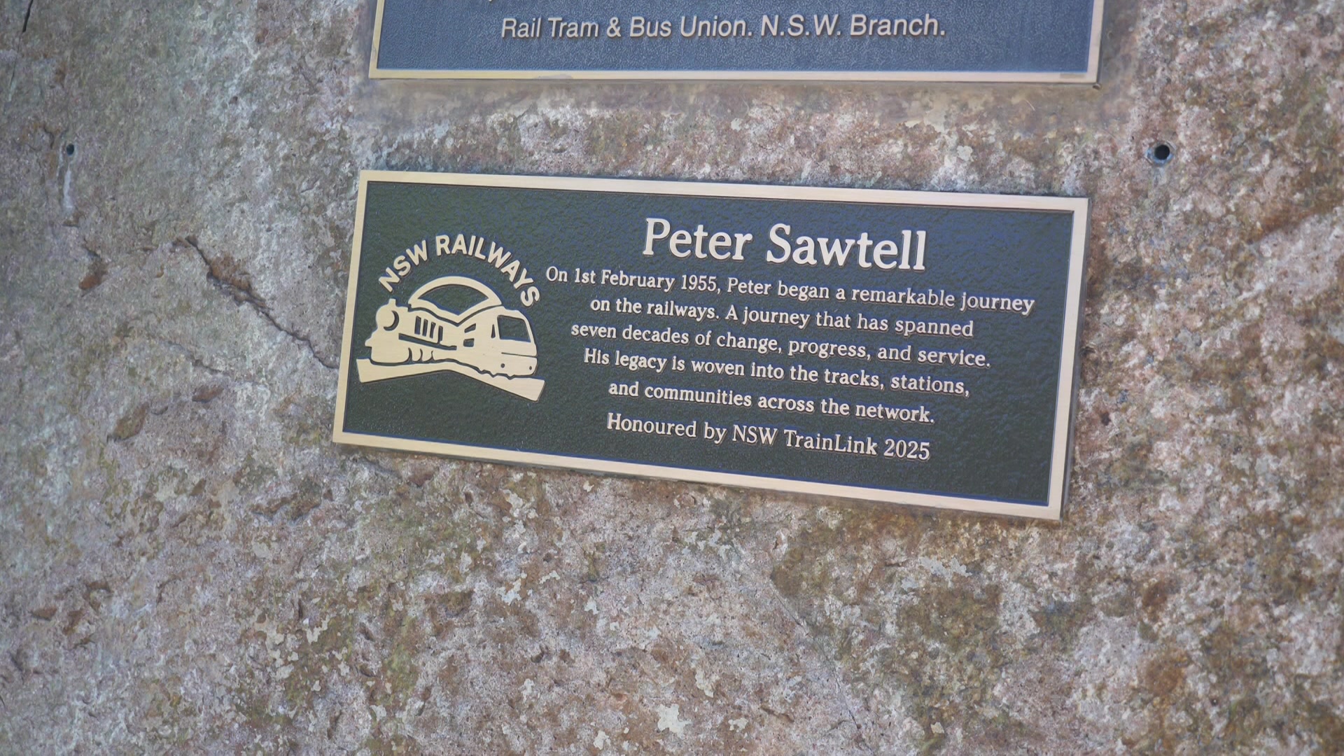 Uma placa em uma rocha com uma inscrição sob o título Peter Sawtell e o logotipo da NSW Railways.