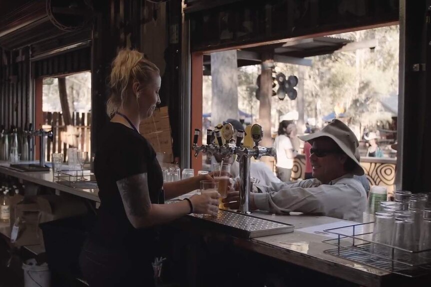 A woman pours a beer while a male customer watches.