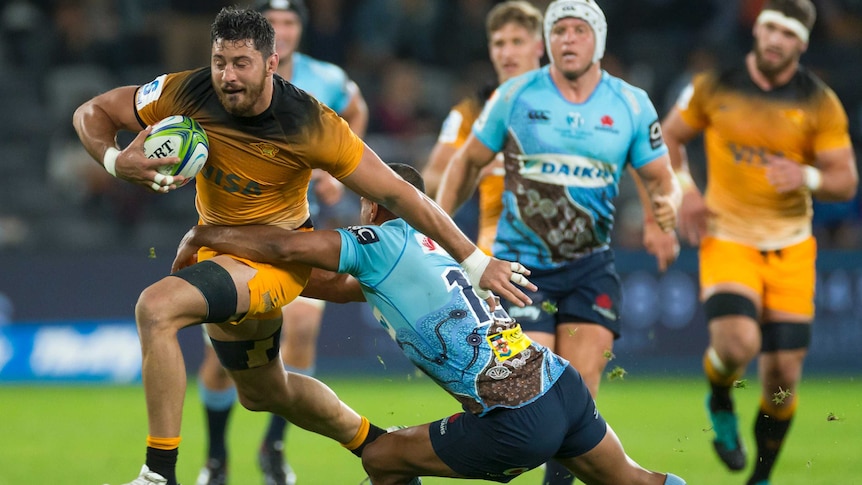 A Jaguares rugby union plays runs with the ball under his right arm as he fends off a tackler.