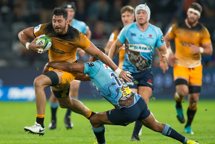 A Jaguares rugby union plays runs with the ball under his right arm as he fends off a tackler.