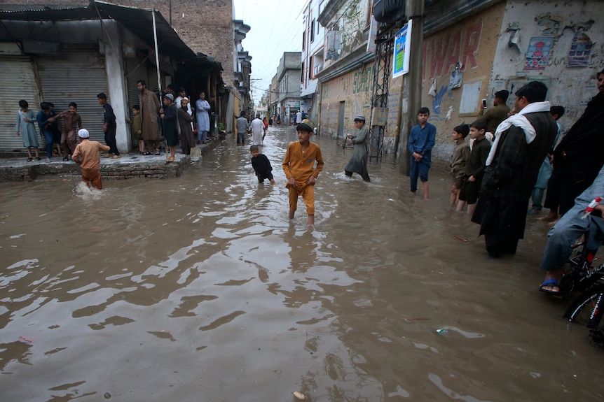 A child wades through a flooded street as other people watch on