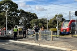A train stopped at a station near a crossing with police standing around the pedestrian crossing