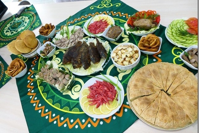 Plates of food including fish, meat and fruit, on a colourful cloth.