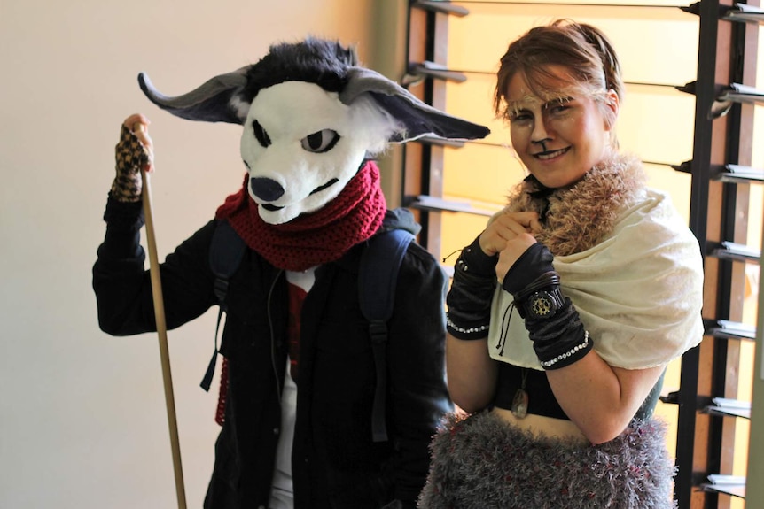 A person wearing a dog head mask and a woman dressed as a fawn stand in front of a window