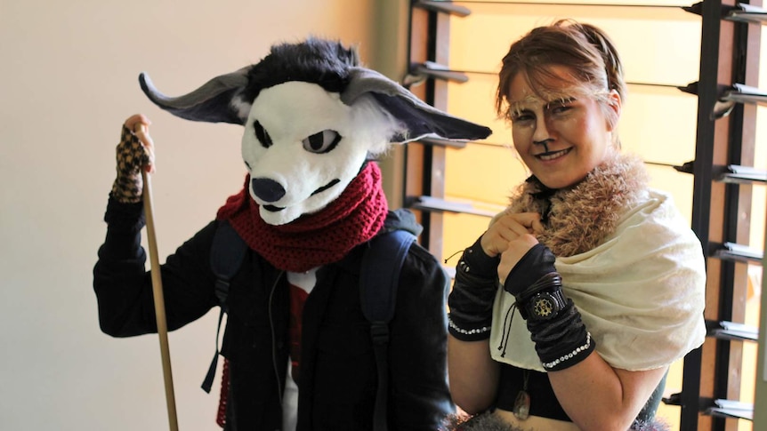 A person wearing a dog head mask and a woman dressed as a fawn stand in front of a window