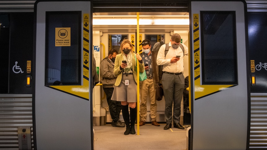 People wear masks pictured through the doors of a train