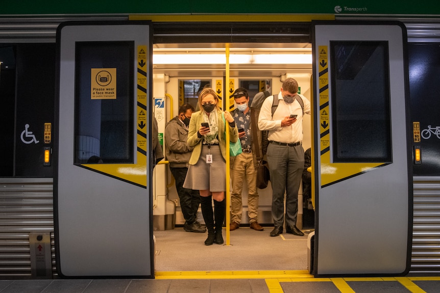 People wear masks pictured through the doors of a train