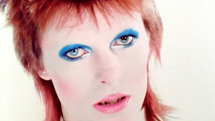 A young David Bowie wears bright make-up 