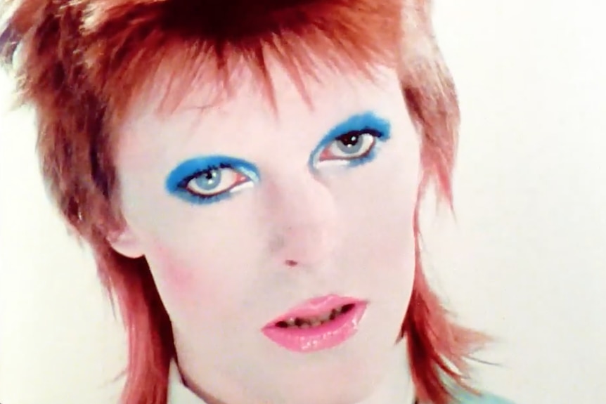A young David Bowie wears bright make-up 