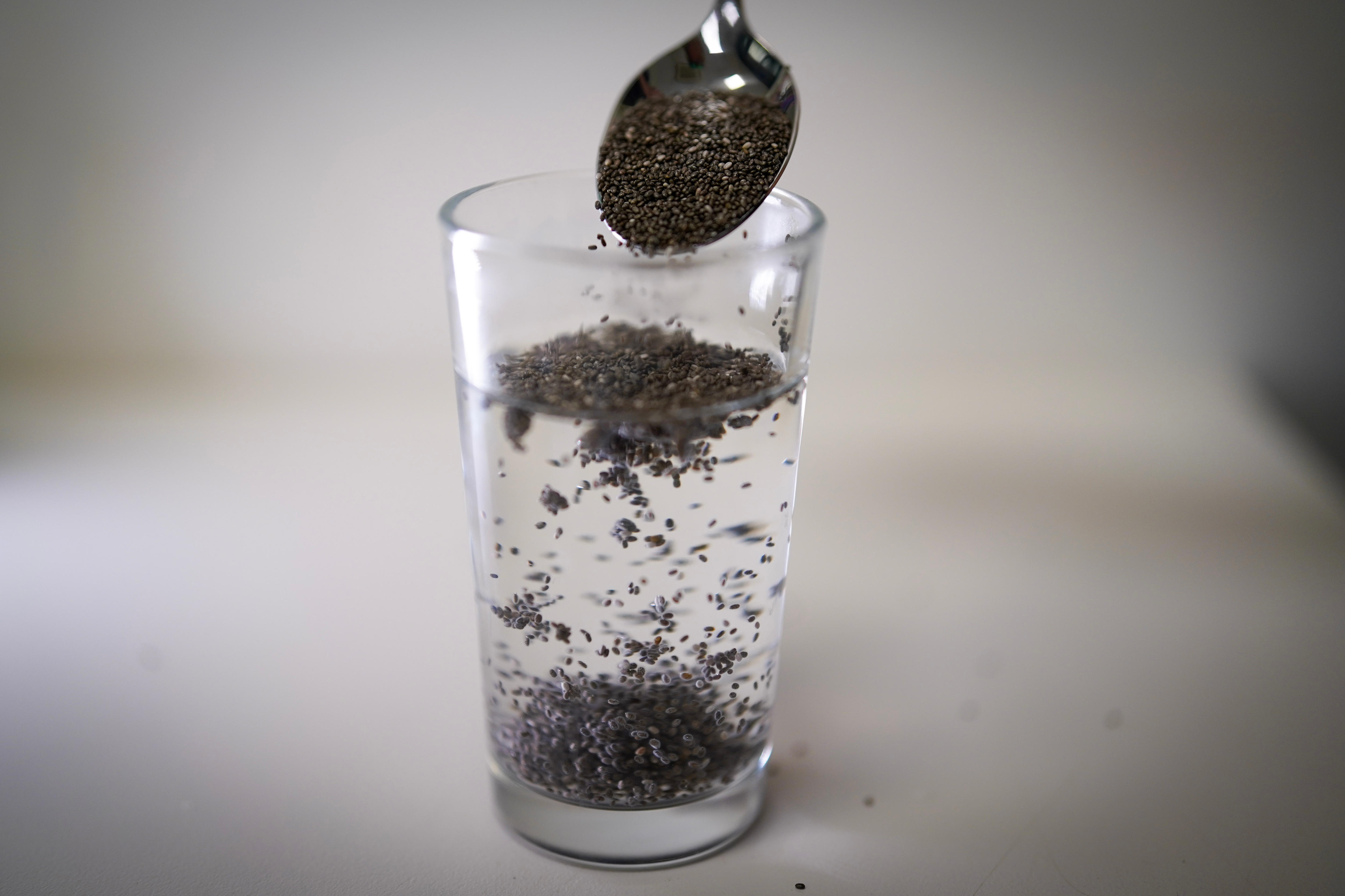 Copo de água com sementes de chia derramado com uma colher.