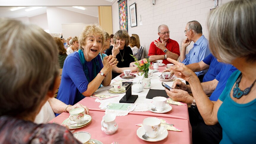 A group of older men and women sit around a table having tea for a story on share housing when retired.
