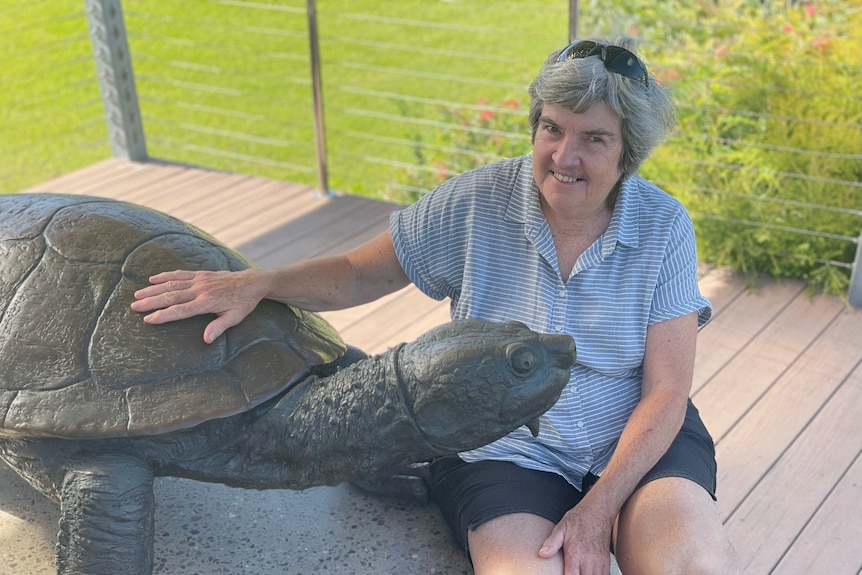 Lady sits smiling next to a turtle sculpture 