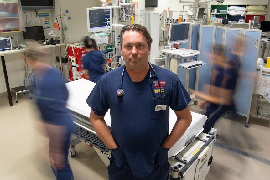 A man wearing blue scrubs stands in an operating room
