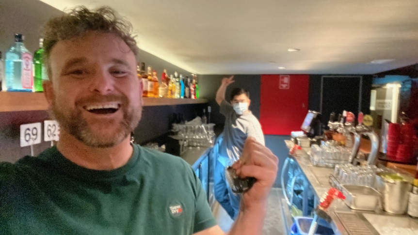 A man smiles in a selfie taken as he's working behind the bar