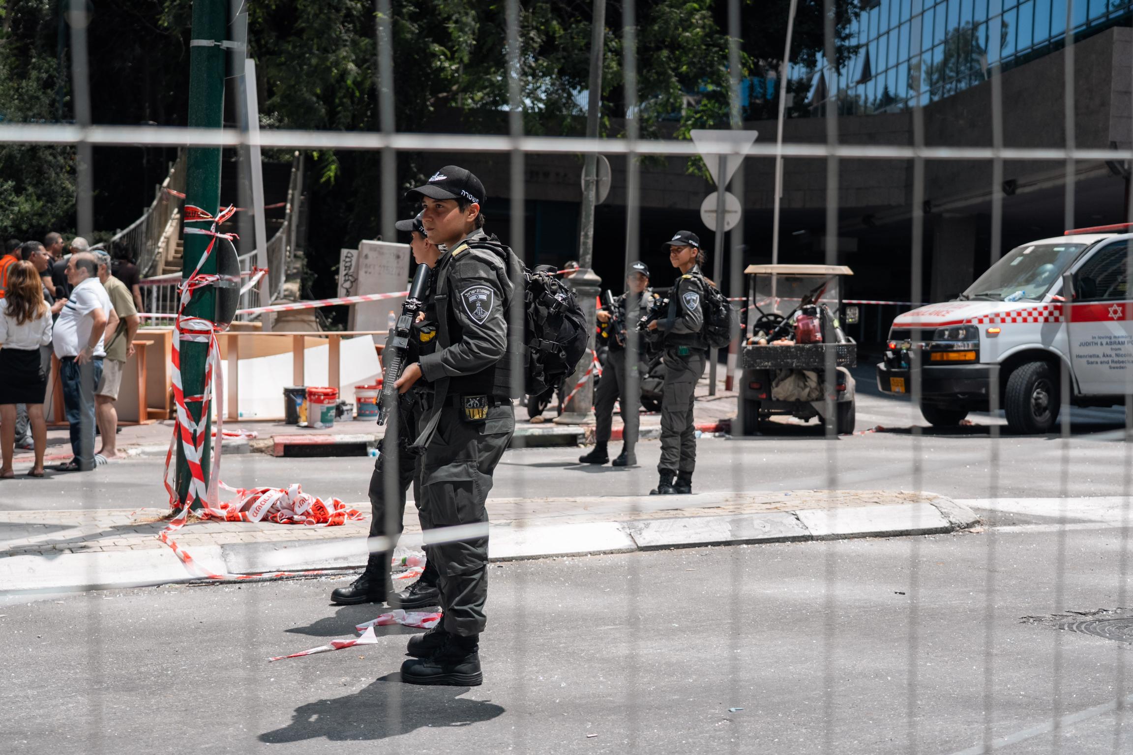 People in army gear stand behind a fence in front of a damaged building. 