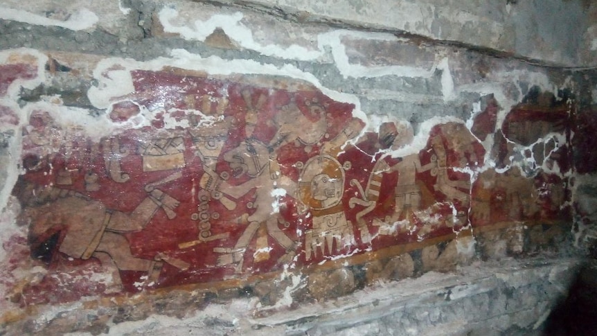 A red, yellow and orange painting on the wall of a tomb depicticing stylised humans and animals.