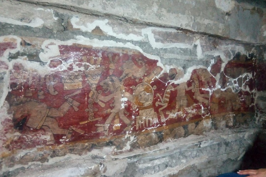 A red, yellow and orange painting on the wall of a tomb depicticing stylised humans and animals.